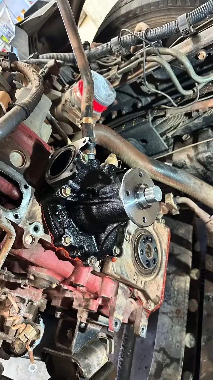 The front of a red-block diesel with a black water pump and fresh gasket surface.