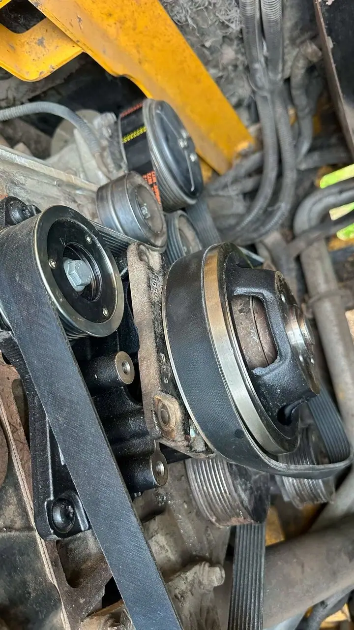 A serpentine belt running over tensioner and drive pulleys on the underside of a yellow machine.