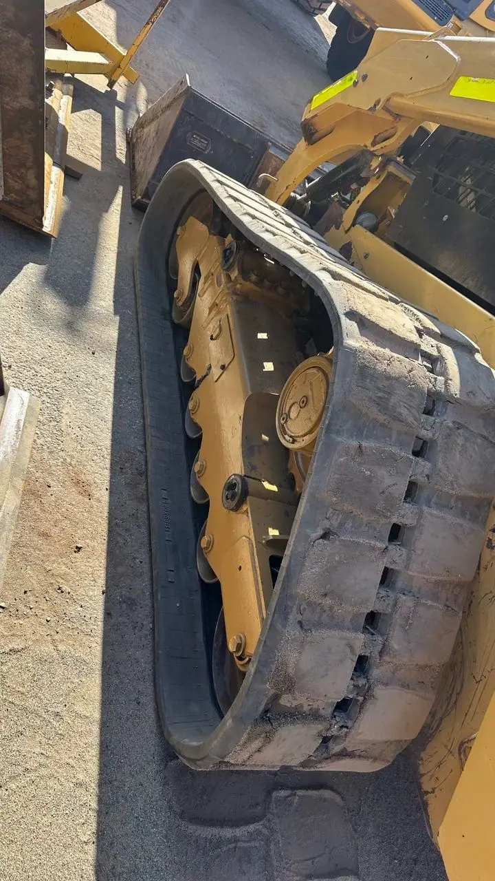 A yellow Cat skid steer with its rubber track and undercarriage exposed beside it.