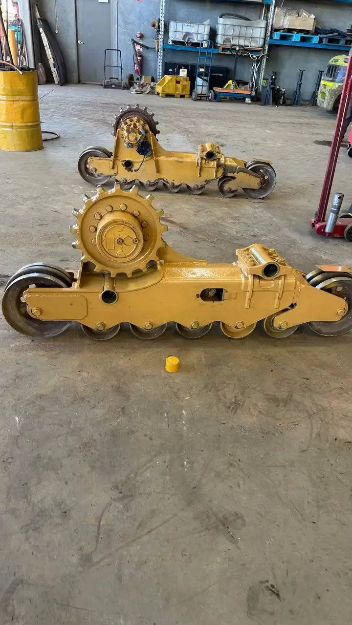 Two yellow undercarriage frames with sprockets and rollers lying on a workshop floor.